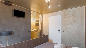 A modern bedroom with a large bed, a bedside table, a mirror, and a TV mounted on the wall.