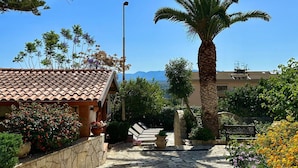 A stone pathway leading to a building with a tiled roof, surrounded by various plants and a palm tree. - Charming Holiday Home Near Sea (Castellammare del Golfo)