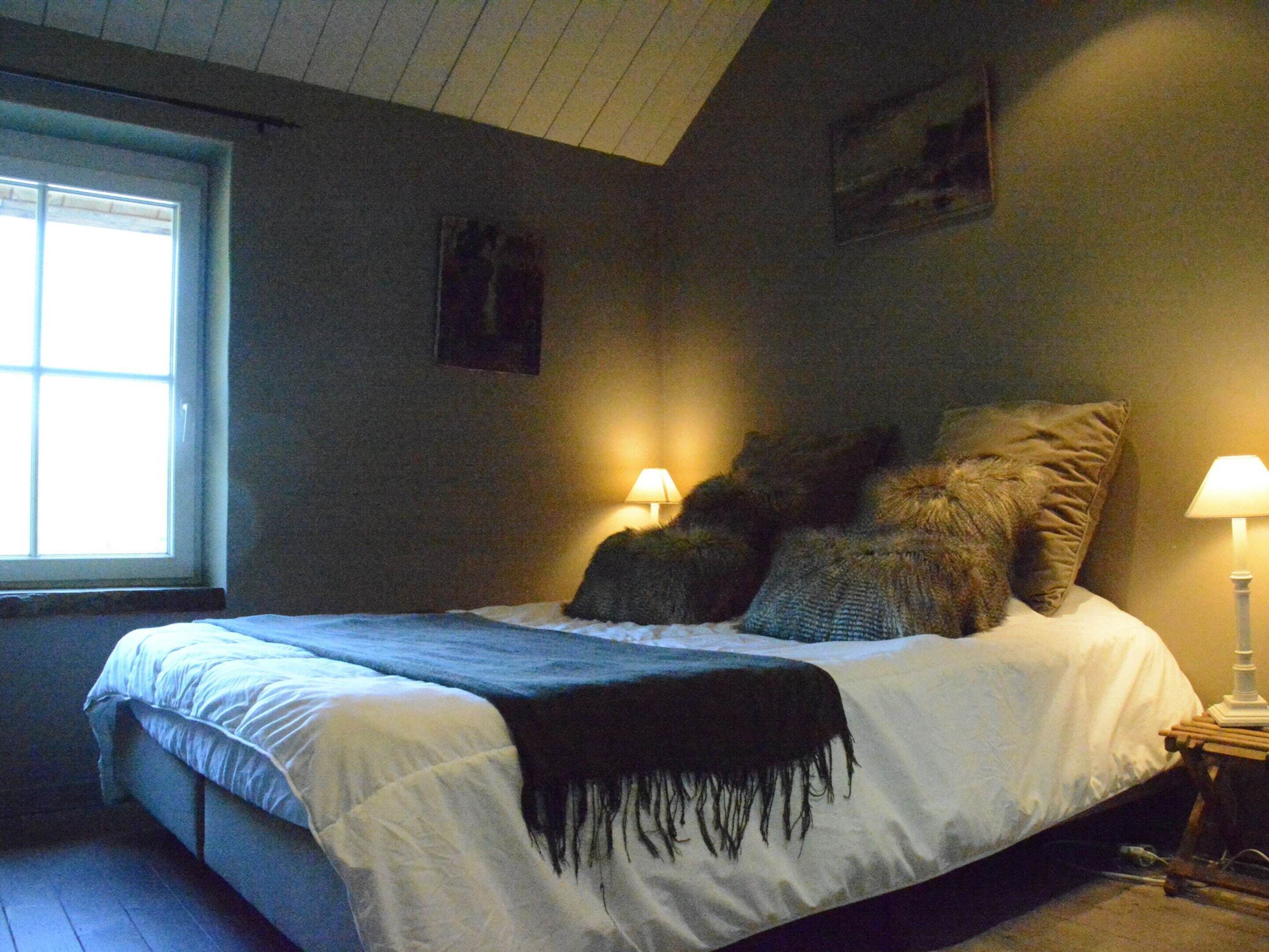 A bedroom with a bed, a window, and a nightstand with a lamp.