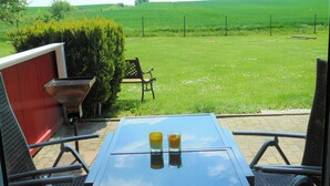 Une terrasse avec une table et des chaises, donnant sur un champ verdoyant.