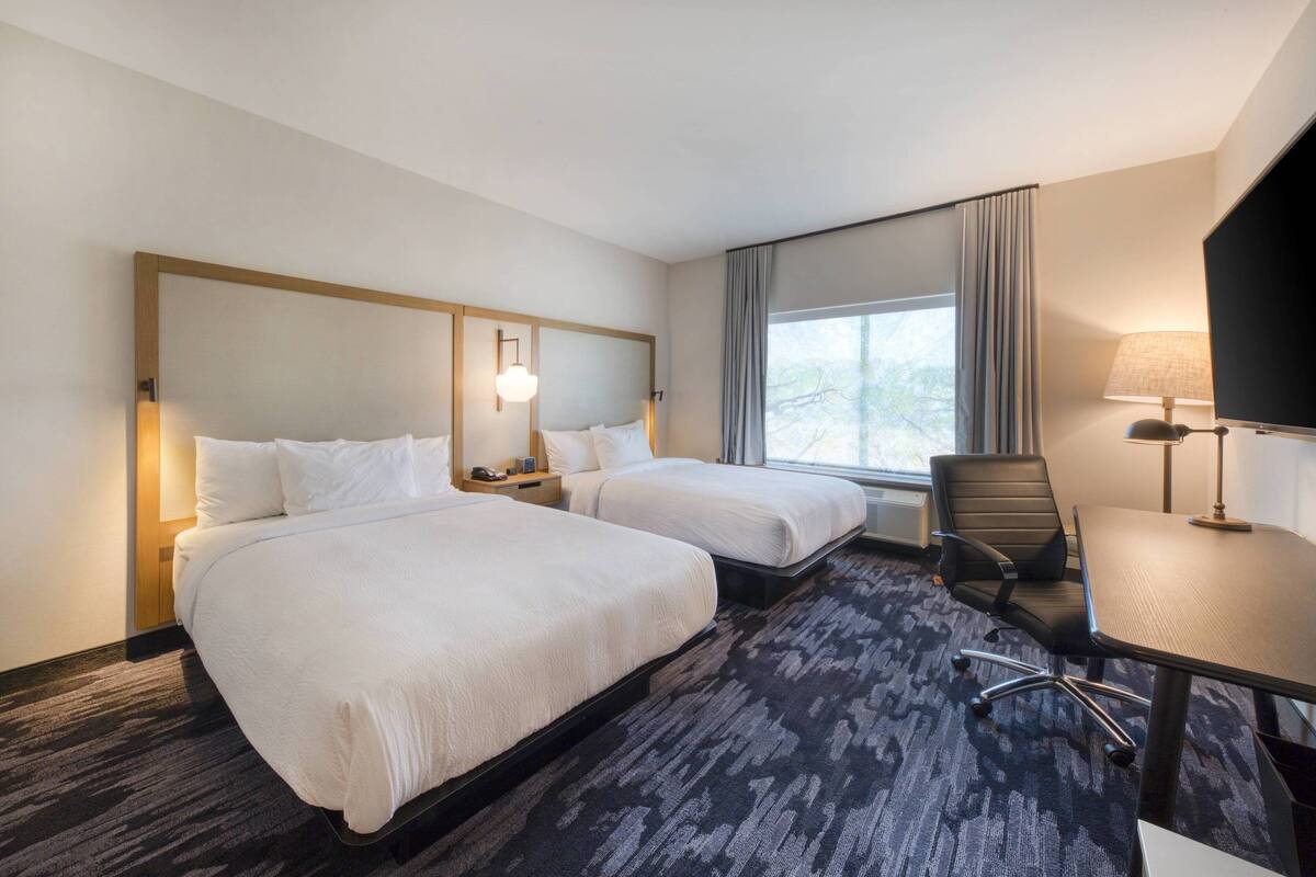 A hotel room with two beds, a desk, a chair, a TV, and a window with curtains.