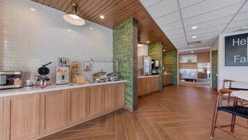 Un área de cocina moderna con mostrador de madera, varios electrodomésticos y una zona de estar con sillas.