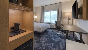 Habitación de hotel con cama, escritorio, silla, cafetera, televisión y ventana con cortinas.