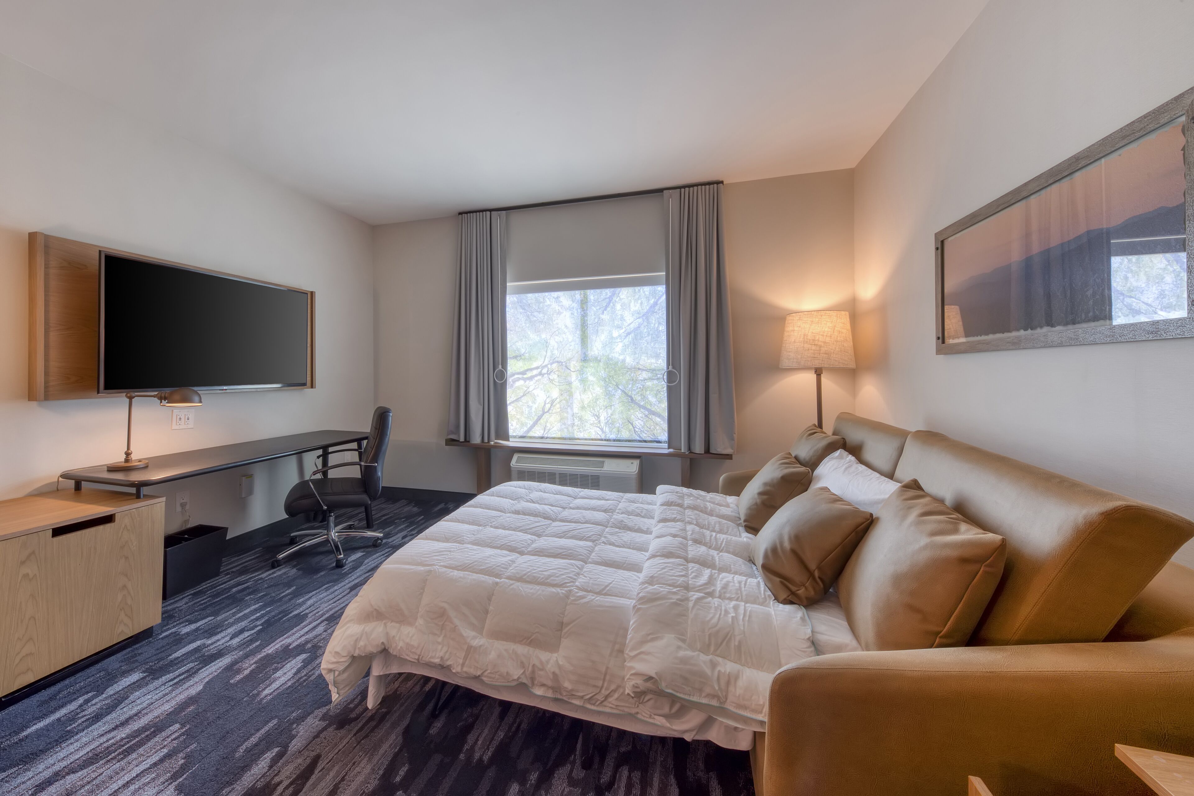 A hotel room with a bed, a desk, a chair, a TV, and a window with curtains.