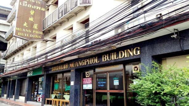 Un immeuble sur lequel on peut lire l’inscription « IMMEUBLE MUANGPHOL » et qui possède de nombreux balcons équipés de climatiseurs.