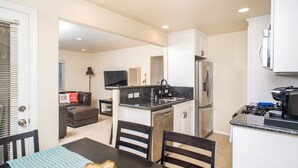 A compact kitchen with a central island, a dining area with a table and chairs, and a living space with a sofa and television. - Belmont Park And  Sea World Boardwalk Bungalow  (San Diego)