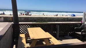 A beach view with a wooden table and chairs, a palm tree, and a clear blue sky. - Belmont Park And  Sea World Boardwalk Bungalow  (San Diego)