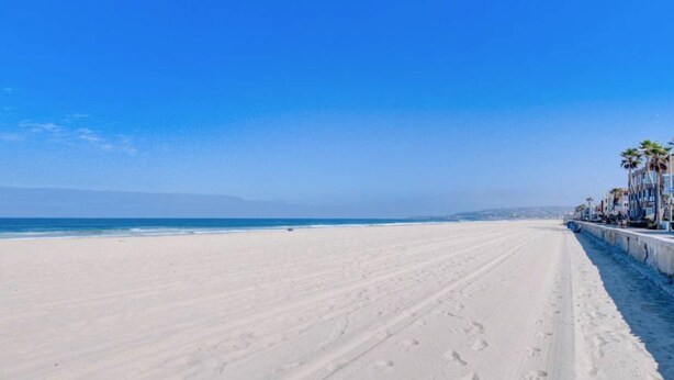 A wide, empty beach with a clear blue sky and a long, straight walkway lined with palm trees and buildings. - Belmont Park And  Sea World Boardwalk Bungalow  (San Diego)