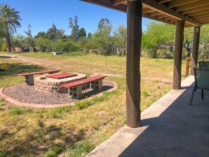 Un’area patio all'aperto con un braciere in pietra, tavoli da picnic e una zona salotto coperta.