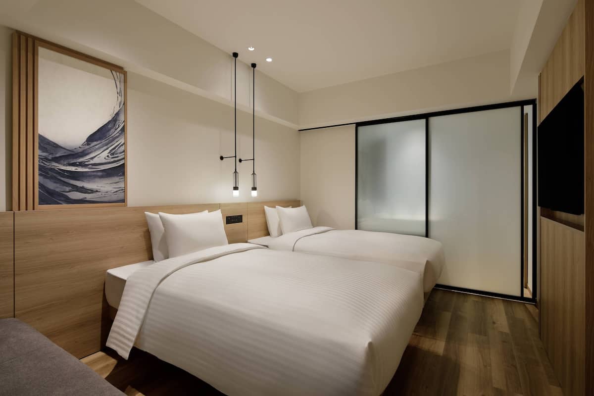 A modern hotel room with two beds, a large artwork on the wall, a sliding door closet, and a mounted television.