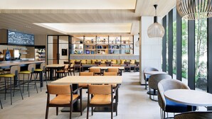 Uma zona de refeições moderna com várias mesas e cadeiras, um bar e uma estante cheia de livros e objetos decorativos.