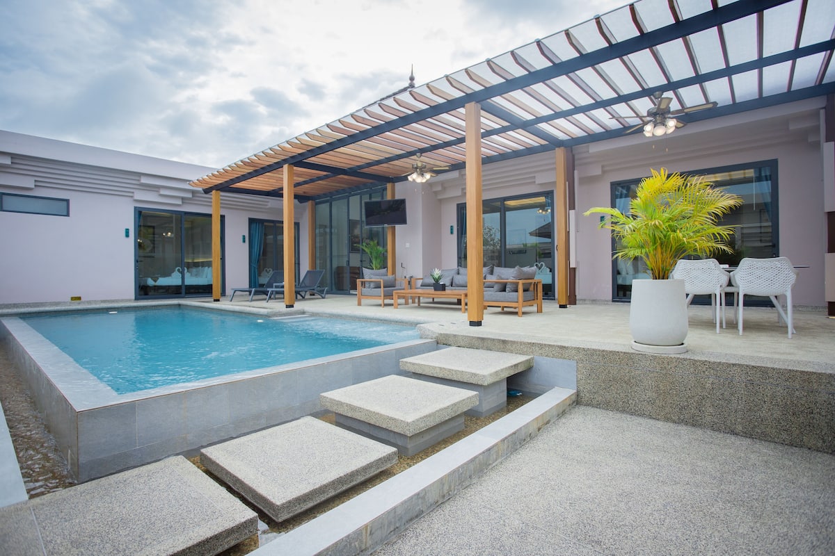 A modern outdoor pool area with a covered seating area, steps leading to the pool, and a potted plant.