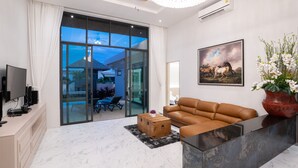 Ein modernes Wohnzimmer mit Ledersofa, Couchtisch, Fernseher und einem großen Fenster mit Vorhängen.