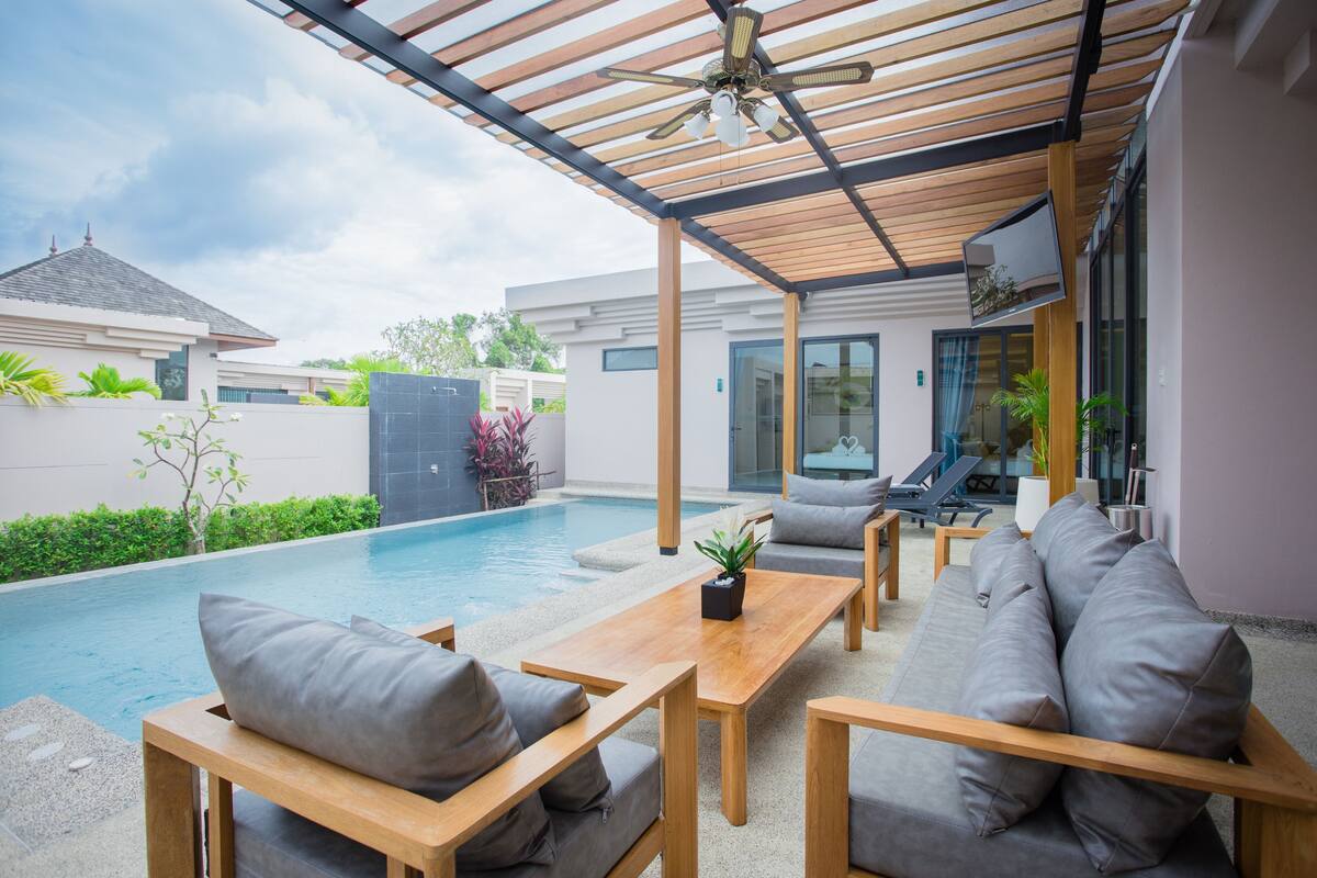 A modern outdoor patio with a pool, wooden furniture, and a ceiling fan.