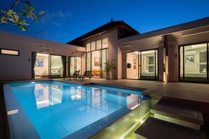Ein modernes Haus mit Pool, großen Glasfenstern und einem gut beleuchteten Innenraum.