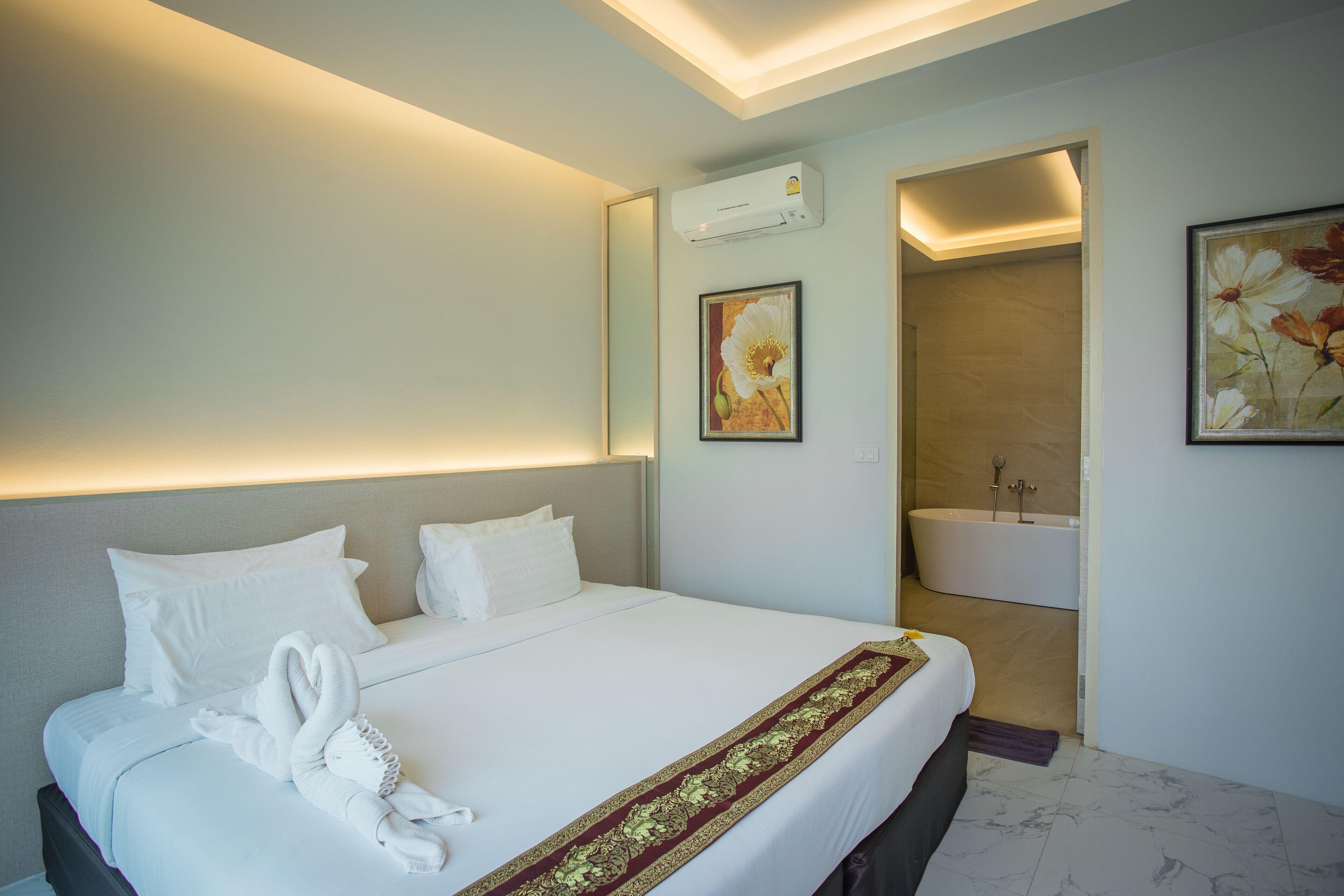 A hotel room with a neatly made bed, a bathroom with a bathtub, and a painting on the wall.