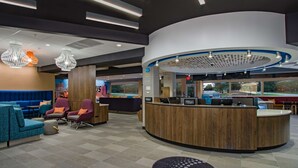 A hotel reception area with a curved wooden counter, seating with colorful cushions, and pendant lighting. - Tru by Hilton Columbus Airport (Columbus)