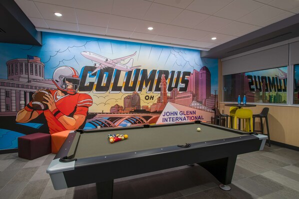 A pool table in a room with a mural of Columbus, OH, and a sign for John Glenn International. - Tru by Hilton Columbus Airport (Columbus)