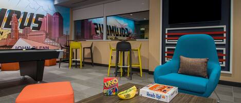 A modern lounge area with a pool table, colorful seating, and various board games.