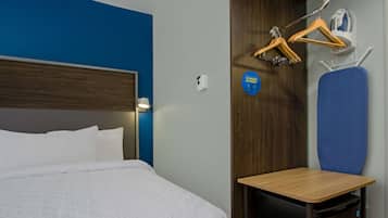 Une chambre d’hôtel comprenant un lit, une petite table, une chaise, un porte-manteau et un panneau indiquant les options de rangement.