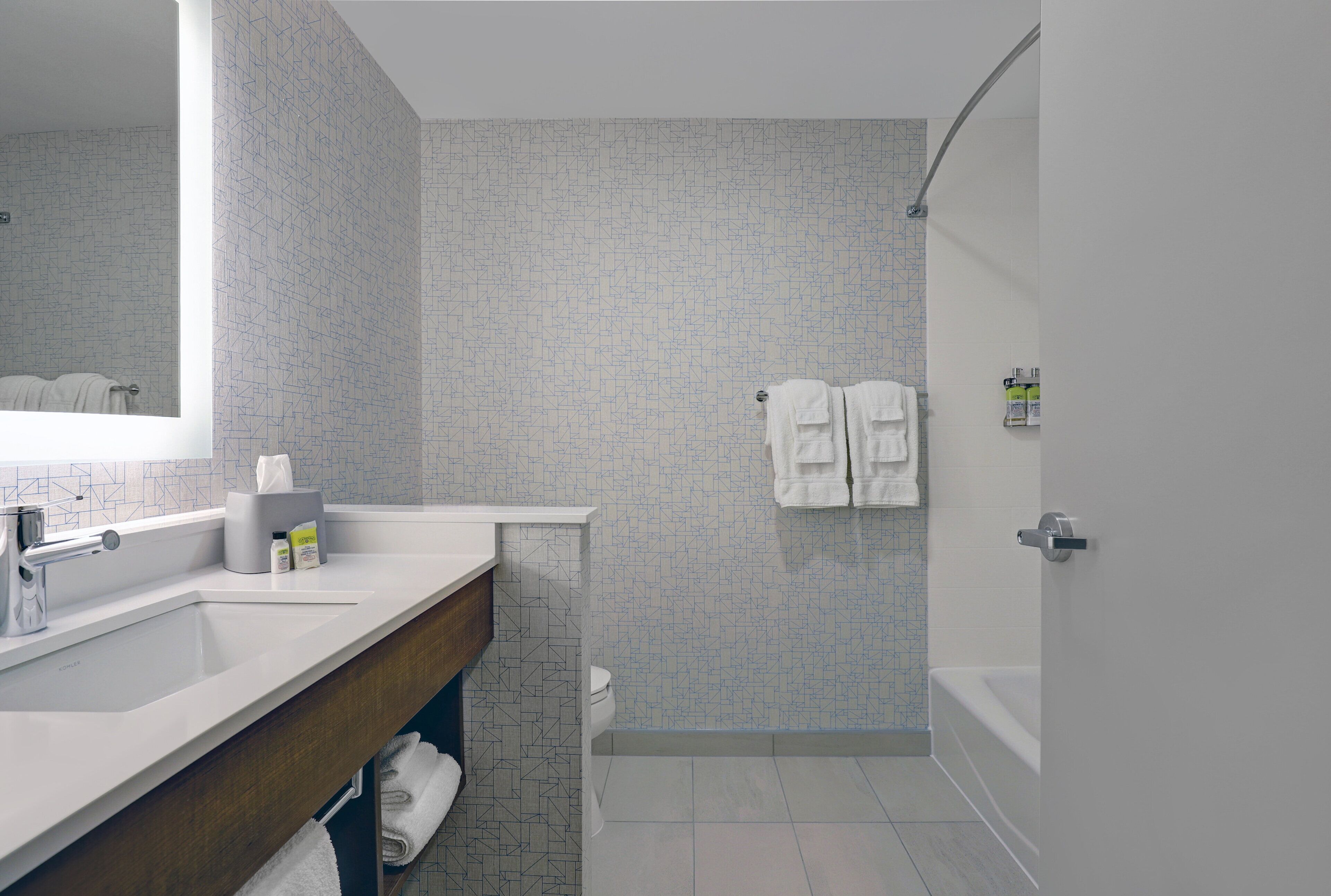 A modern bathroom with a large mirror, two sinks, a toilet, and a bathtub.