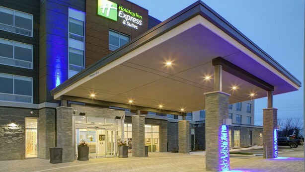 Edificio de Holiday Inn Express & Suites con entrada cubierta, pilares de piedra y fachada bien iluminada.