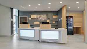 A modern hotel reception area with a minimalist design, featuring two reception desks, a wall-mounted information board, and a Coca-Cola refrigerator. - Holiday Inn Express & Suites Collingwood by IHG (Collingwood)