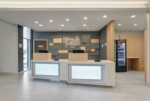 A modern hotel reception area with a minimalist design, featuring two reception desks, a wall-mounted information board, and a Coca-Cola refrigerator. - Holiday Inn Express & Suites Collingwood by IHG (Collingwood)