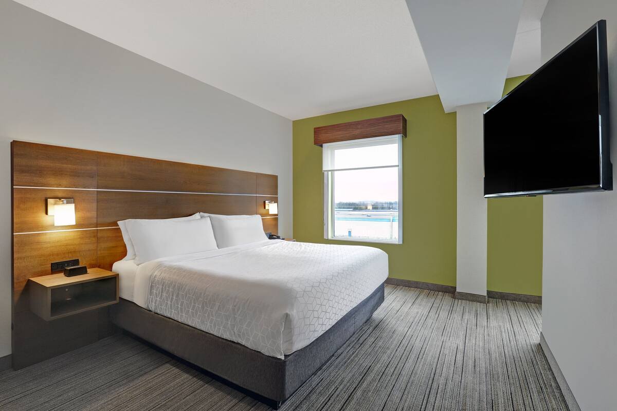 A hotel room with a large bed, a nightstand with a phone, a wall-mounted TV, and a window with a view.