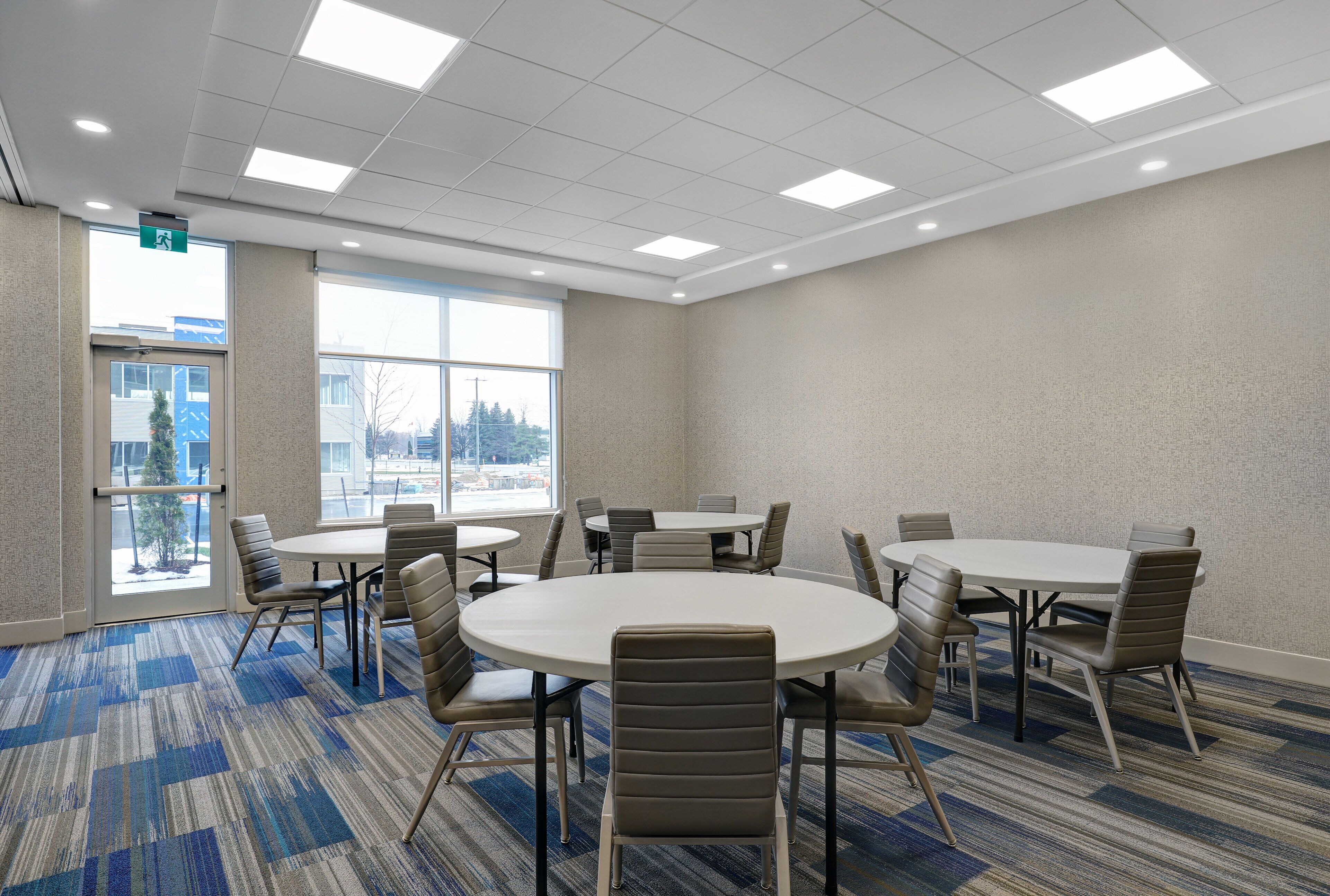 A conference room with round tables and chairs, large windows, and a carpeted floor.