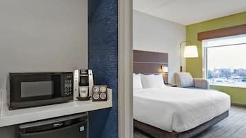 Habitación de hotel con cama, minibar, cafetera y vista a la ciudad.