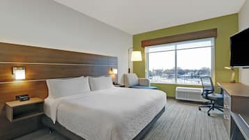 A hotel room with a large bed, a desk, a chair, a TV, and a window with a view of the city.