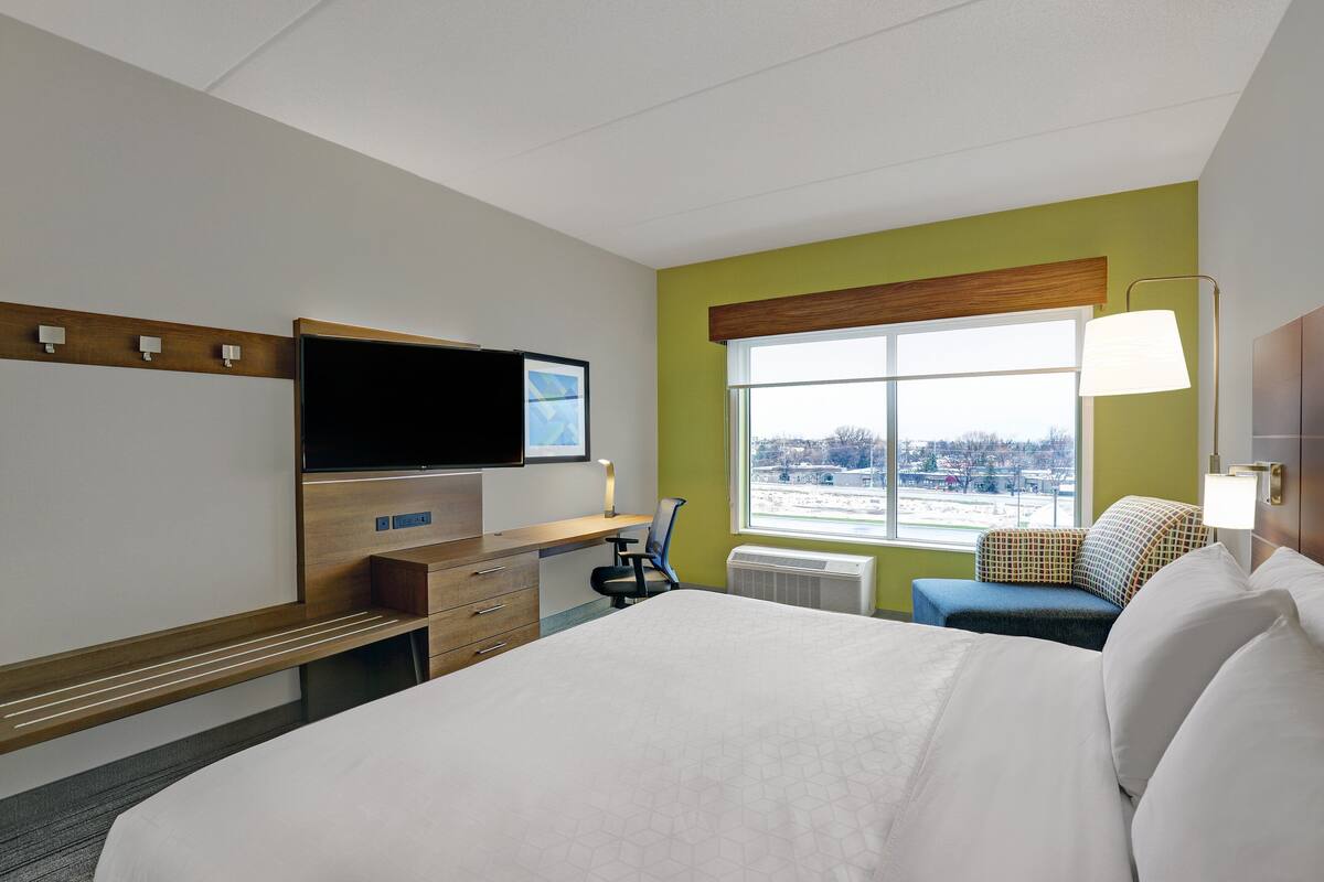 A hotel room with a bed, a desk, a chair, a television, and a window with a view of the city.