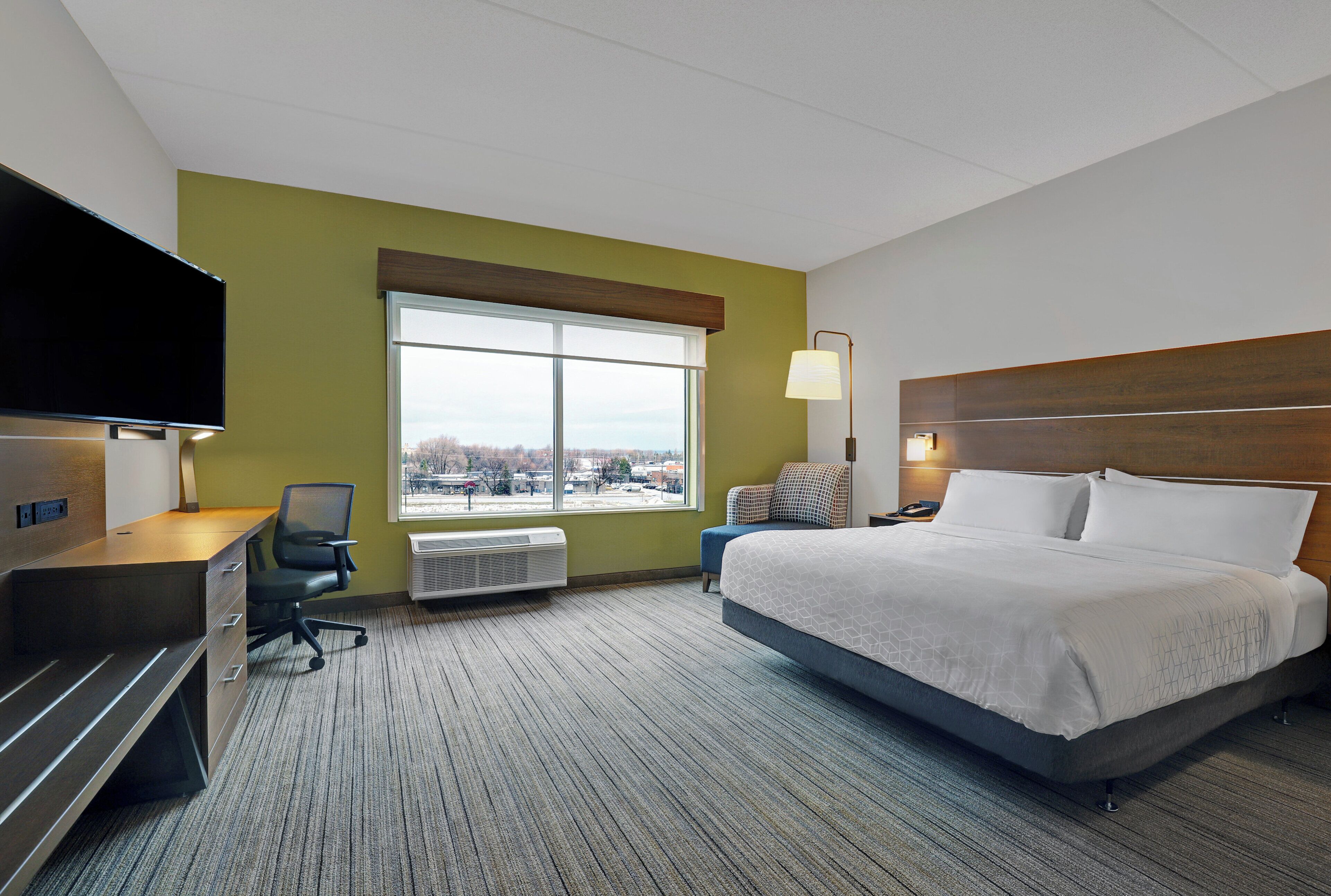 Een hotelkamer met een bed, een bureau, een stoel, een televisie en een raam met uitzicht op de stad.