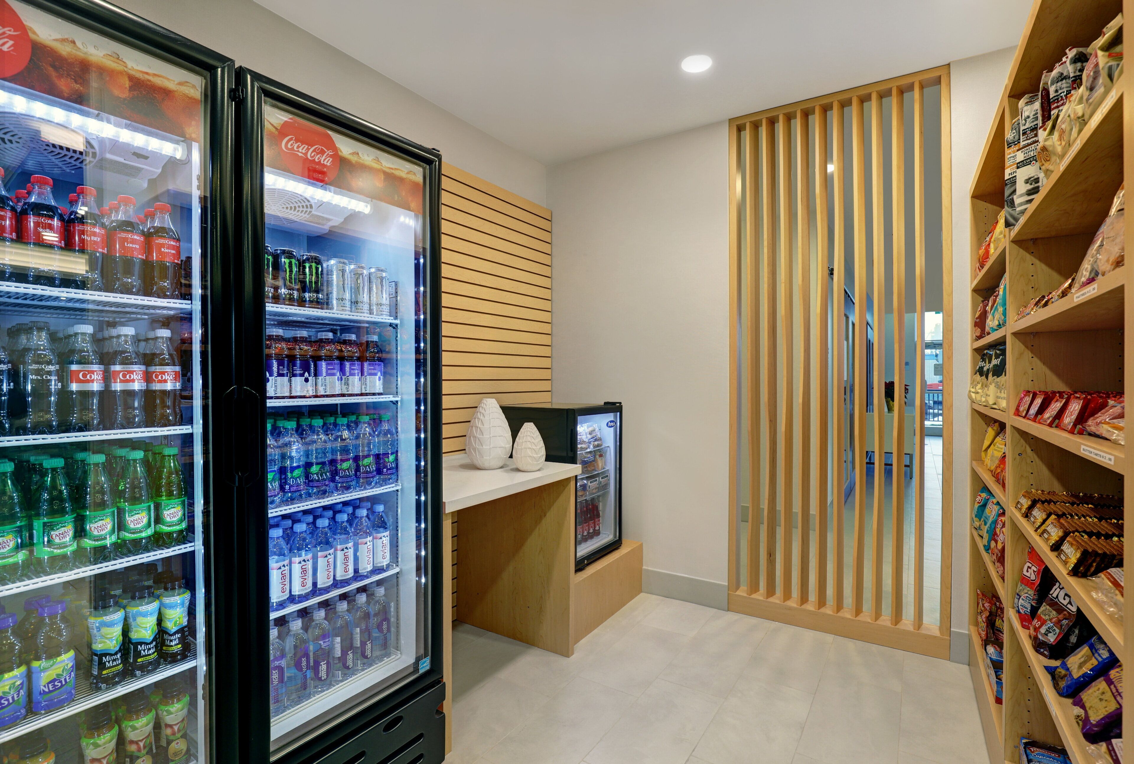 A beverage cooler with various drinks, a snack shelf with packaged goods, and a wooden partition.