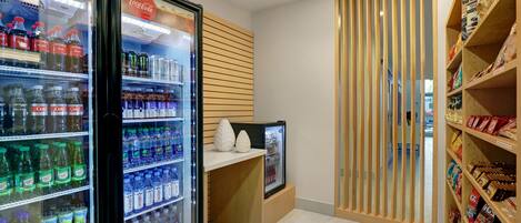 A beverage cooler with various drinks, a snack shelf with packaged goods, and a wooden partition.