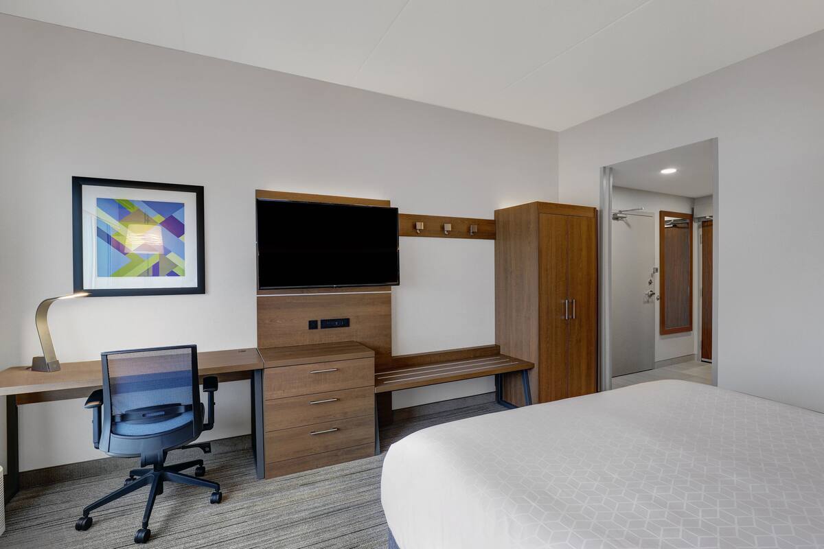 A hotel room with a bed, a desk with a chair, a television, and a wardrobe.