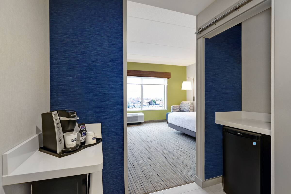 A hotel room with a kitchenette, a bed, a window with a view, and a bathroom.