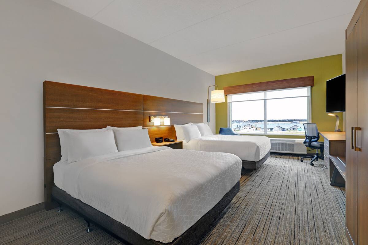 A hotel room with two beds, a desk, a chair, a TV, and a large window.