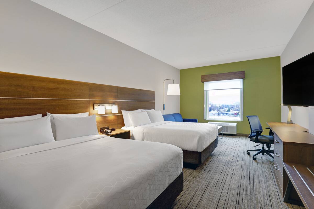 A hotel room with two beds, a desk, a chair, a TV, and a window with a view.