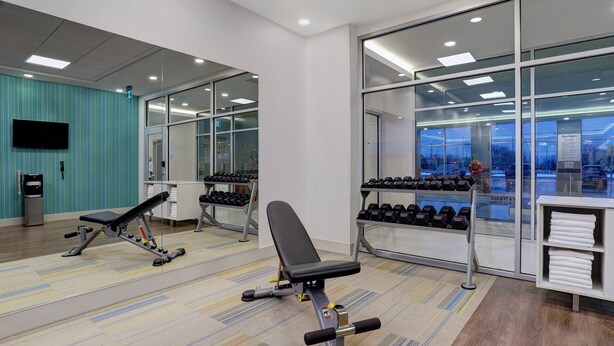A gym with exercise equipment, mirrors, and a view of the city through large windows. - Holiday Inn Express & Suites Collingwood by IHG (Collingwood)