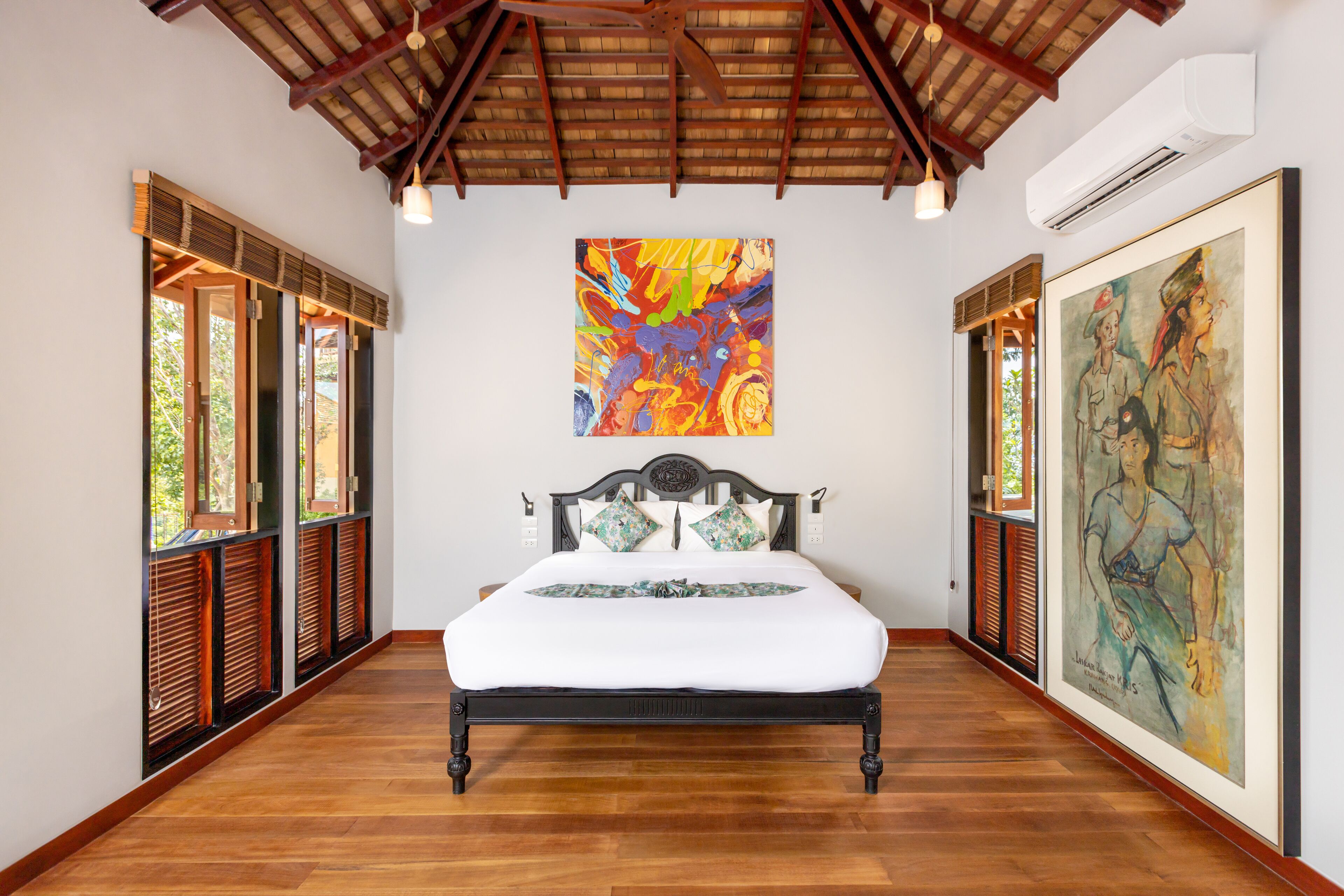 A room with a bed, wooden floor, and artwork on the walls.