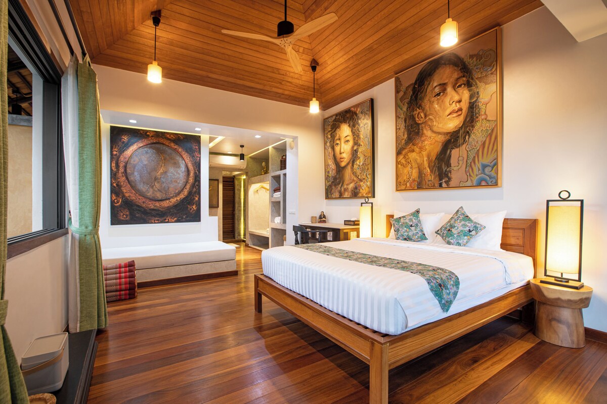 A spacious bedroom with a wooden bed, a large painting on the wall, and a view of a bathroom.