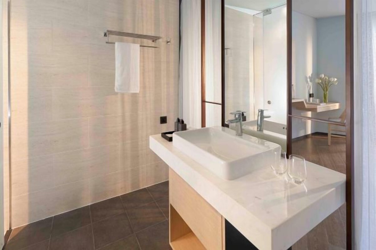 Un baño moderno con un lavamanos grande de color blanco, un espejo y un perchero para toallas.