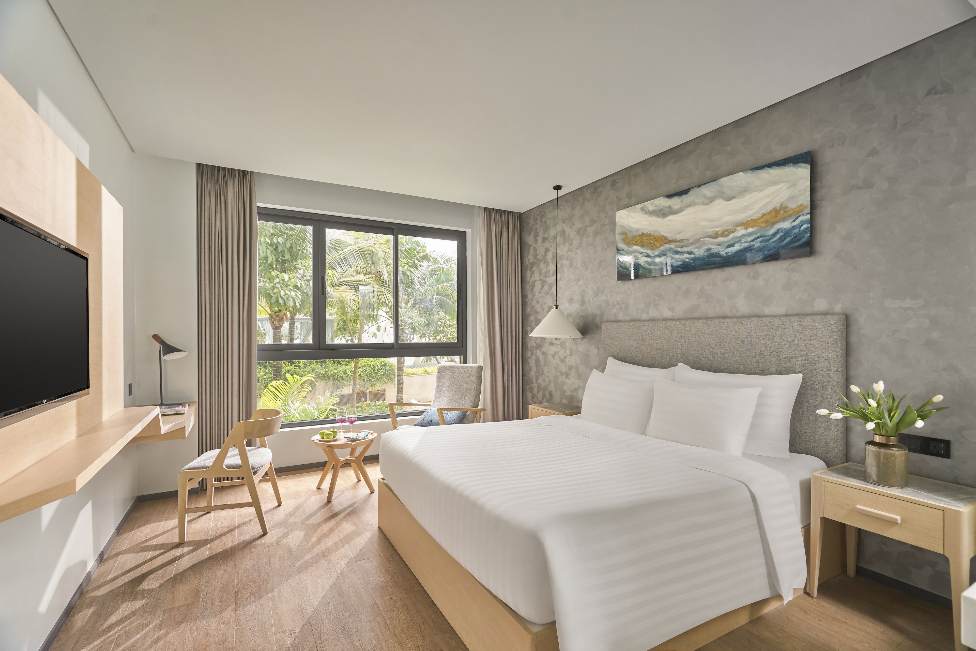 Una habitación de hotel moderna con una cama grande, un escritorio, una silla, un televisor y una ventana con cortinas.