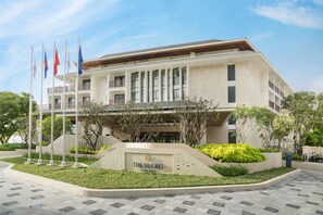 A modern hotel with a prominent entrance, multiple flags, and a landscaped garden area. - The Secret Con Dao (Ho Chi Minh City)