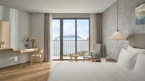 A hotel room with a large bed, a desk with a chair, a small table with flowers, and a view of the sea through a balcony. - The Secret Con Dao (Ho Chi Minh City)