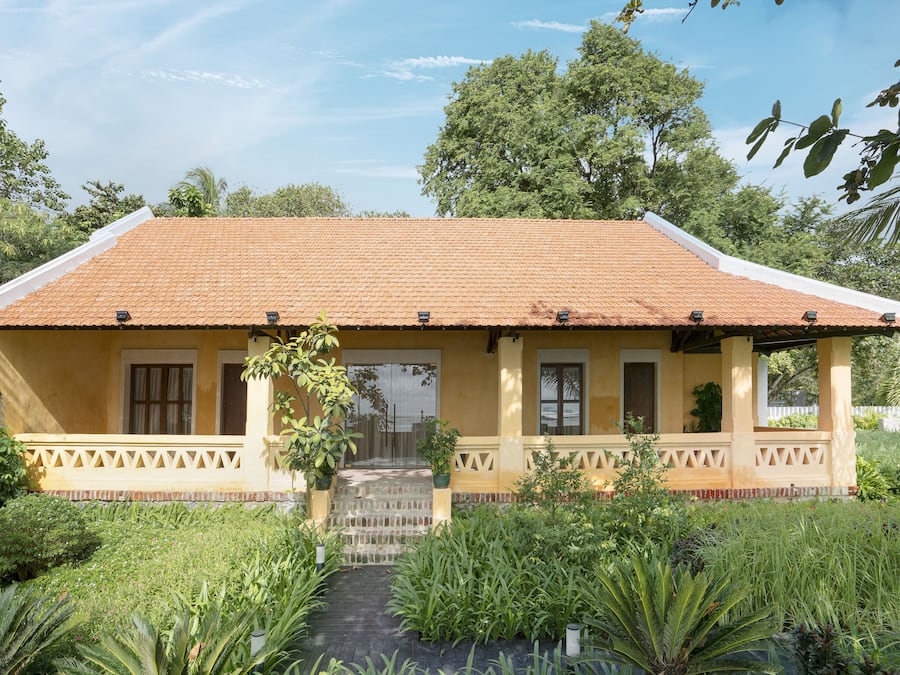 A yellow building with a tiled roof, a covered porch, and a garden with various plants.