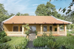 A yellow building with a tiled roof, a covered porch, and a garden with various plants.