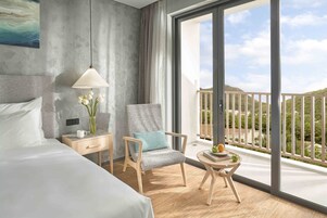 A hotel room with a bed, a chair, a nightstand, a lamp, and a view of the balcony.